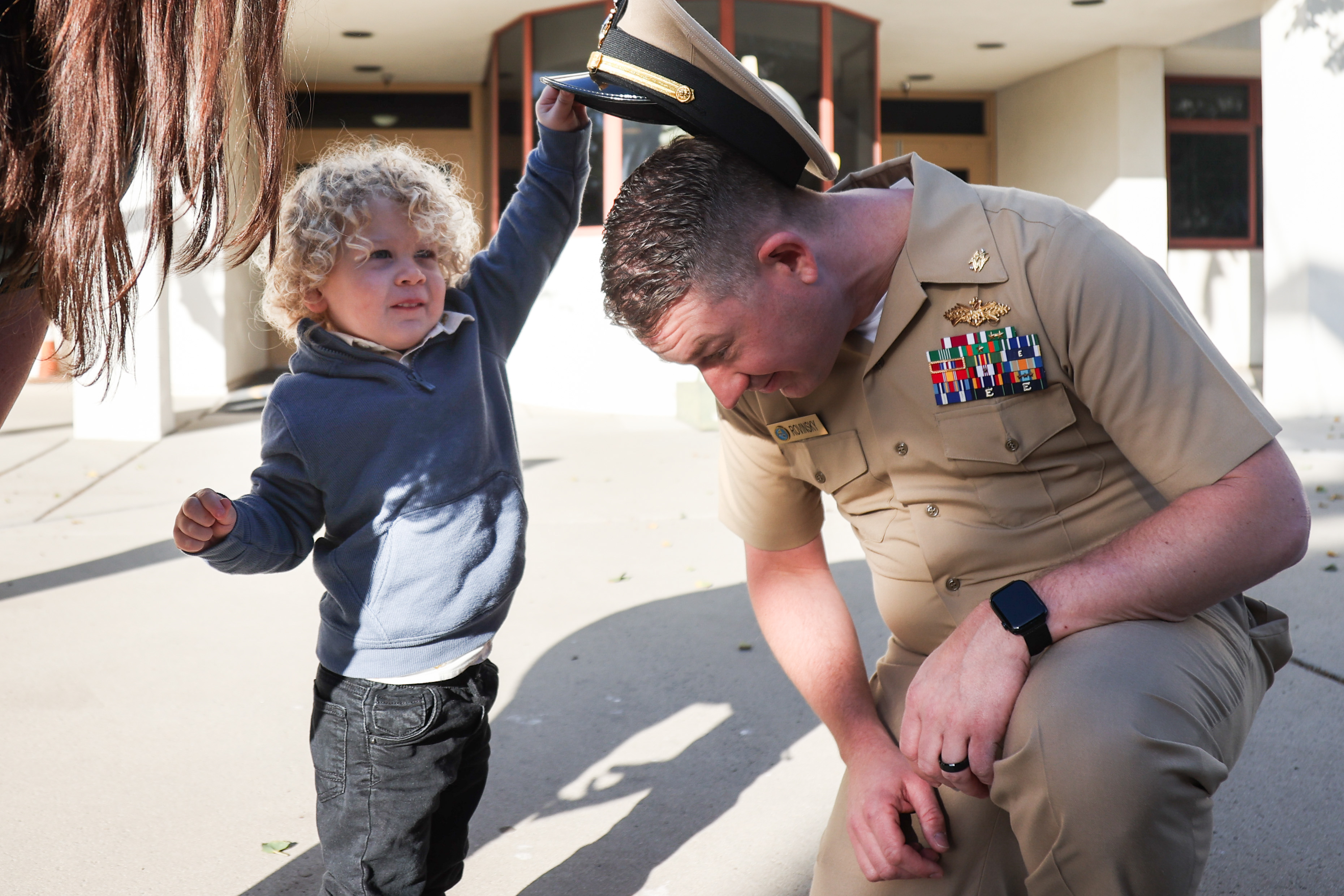 In a photo taken by Petty Officer 1st Class Justin Rayburn a young boy takes a hat off a U.S. service member.